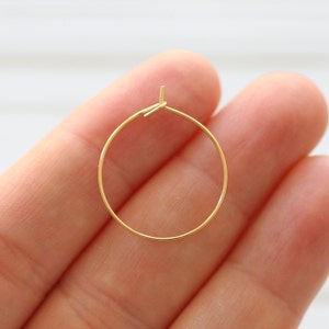 Puede incluir: Un par de pendientes de aro de oro. Los aros son finos y delicados, y est&aacute;n hechos de un metal liso.