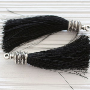 May include: Two black tassel trims with silver metal tips. The tassels are made of soft, fine fibres and have a decorative, ornate metal tip.