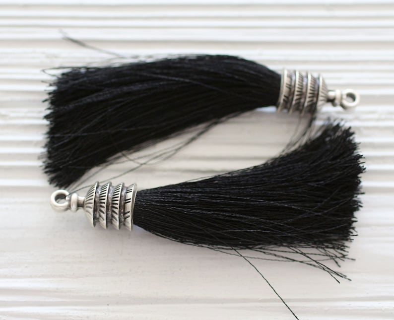 May include: Two black tassel trims with silver metal tips. The tassels are made of soft, fine fibres and have a decorative, ornate metal tip.