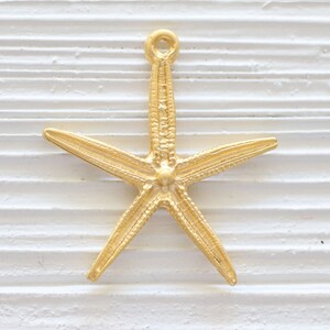 May include: Gold-toned metal starfish charm with a loop at the top for hanging. The starfish has a detailed, textured surface.