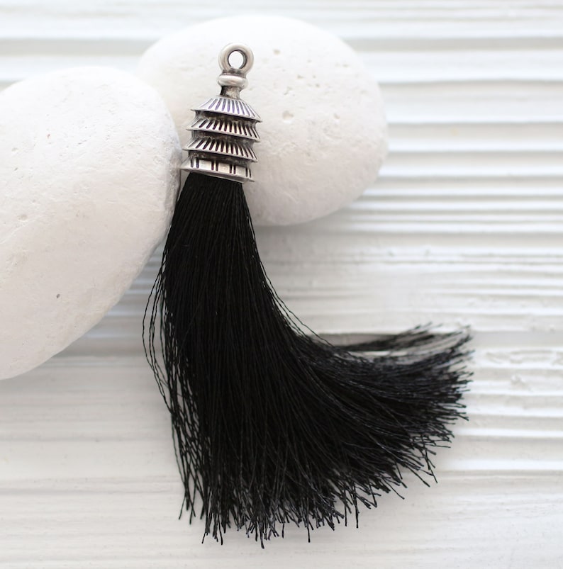 May include: A black tassel with a silver pagoda-shaped top. The tassel is hanging from a white surface.