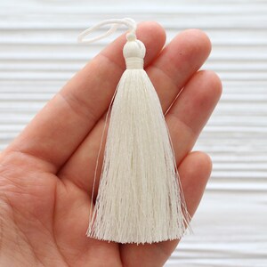 May include: A white tassel with a loop at the top. The tassel is made of soft, silky threads and is approximately 2 inches long.