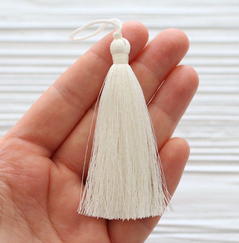 May include: A white tassel with a loop at the top. The tassel is made of soft, silky threads and is approximately 2 inches long.