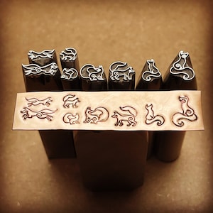 May include: A set of nine metal stamps featuring various fox designs. The stamps are arranged in a row on a wooden surface. The stamps are used for creating impressions in metal, leather, or other materials.