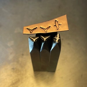 May include: Four metal stamps with bird designs. The stamps are arranged in a row, with the largest stamp at the top and the smallest stamp at the bottom. The stamps are made of a dark metal and have a shiny finish. The bird designs are raised and have a light metal finish.