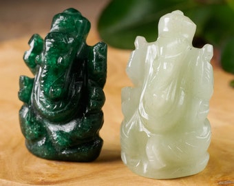 Puede incluir: Dos pequeñas estatuas talladas de la deidad hindú Ganesha. Una es de color verde esmeralda oscuro, la otra verde jade pálido. Ambas están sentadas con las manos en posición de bendición. Las estatuas se exhiben sobre una superficie de madera.