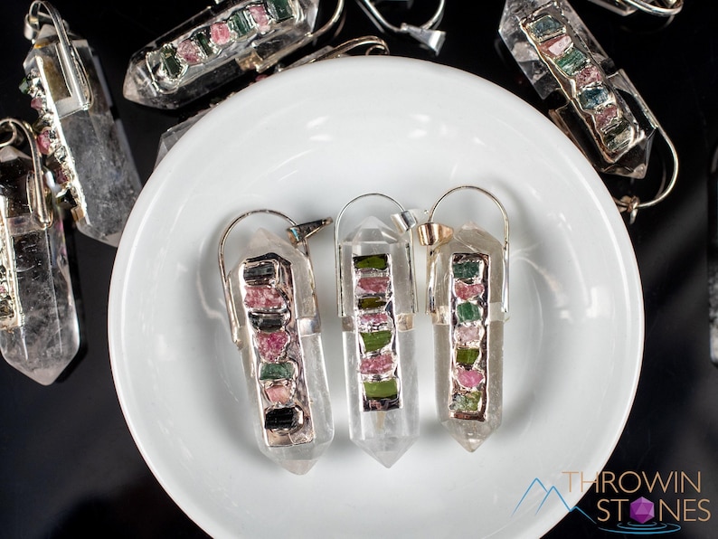 This crystal pendant features a clear Quartz gemstone, showcasing its transparent beauty and amplifying properties. Surrounding the Quartz are seven, green and pink Tourmaline gemstone accent crystals.