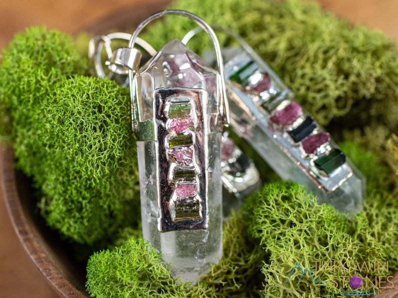 This crystal pendant features a clear Quartz gemstone, showcasing its transparent beauty and amplifying properties. Surrounding the Quartz are seven, green and pink Tourmaline gemstone accent crystals.