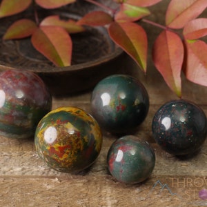 Natural Bloodstone crystal sphere, with wooden stand. This semi-precious, crystal ball is green with red hematite inclusions. Each crystal sphere is beautifully handcrafted, ethically sourced and comes with a wooden stand. This Listing has variations