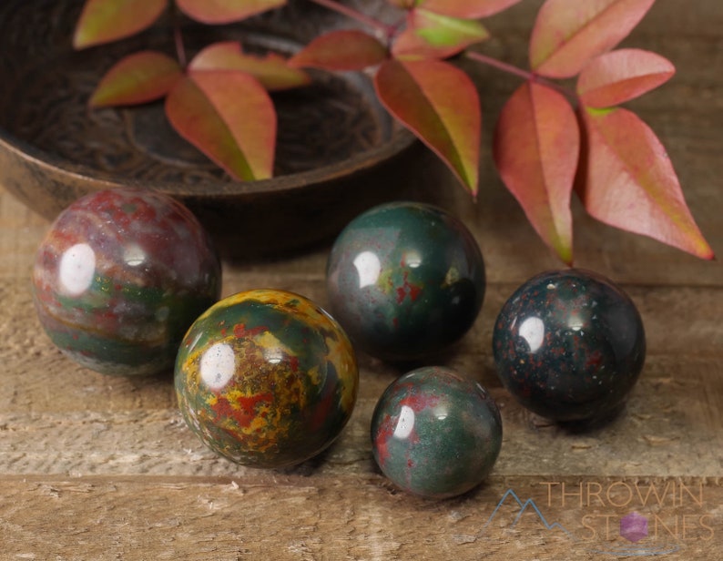 Natural Bloodstone crystal sphere, with wooden stand. This semi-precious, crystal ball is green with red hematite inclusions. Each crystal sphere is beautifully handcrafted, ethically sourced and comes with a wooden stand. This Listing has variations