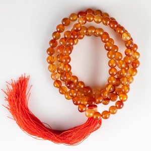 These red orange Carnelian necklaces have 108 sphere beads with a red tassel.  
Crystals are nature-made therefore each one is unique in appearance.