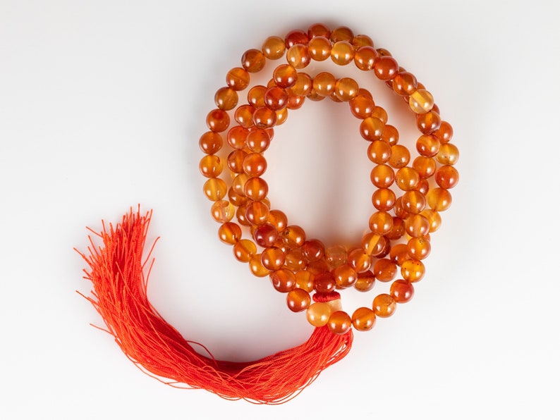 These red orange Carnelian necklaces have 108 sphere beads with a red tassel.  
Crystals are nature-made therefore each one is unique in appearance.