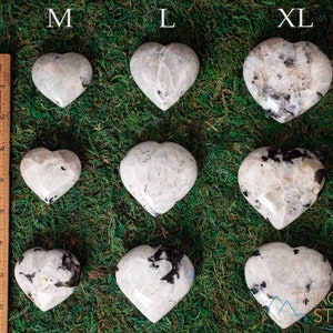 Genuine Moonstone heart shaped crystal. This beautifully hand carved, puffy, palm stone heart, is white with specks of black and rainbow flash. Each crystal heart is unique, and has its own color, shape, and pattern. This listing has variations.