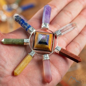 Könnte beinhalten: Ein siebenspitziges Chakra-Set aus Kristallen mit einer Pyramide in der Mitte. Die Spitzen bestehen aus Amethyst, klarem Quarz, grünem Aventurin, gelbem Citrin, rotem Jaspis, Rosenquarz und Lapislazuli.