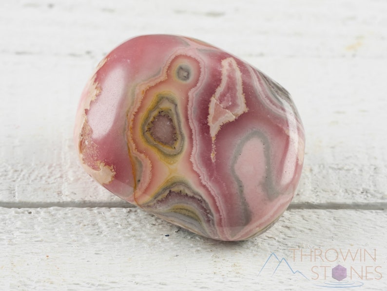 Rhodochrosite Tumbled Stones. These polished crystals are pink with yellowish grey white and brown bands. Each crystal is unique in color and you will receive 1 stone that is 0.7 to 1.7 inches long and weighs 6 to 65 grams. Listing has variations.