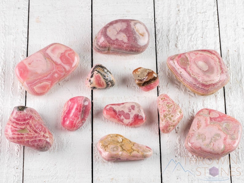 Rhodochrosite Tumbled Stones. These polished crystals are pink with yellowish grey white and brown bands. Each crystal is unique in color and you will receive 1 stone that is 0.7 to 1.7 inches long and weighs 6 to 65 grams. Listing has variations.