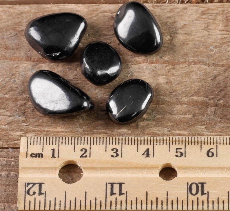 Hematite Tumbled Gemstones. These ethically sourced, semi precious, crystals are black with a polished finish. You will receive 5 stones that are 1.7 to 2.4 centimeters in length and weigh 25 to 35 grams total. Each stone is unique in shape and color