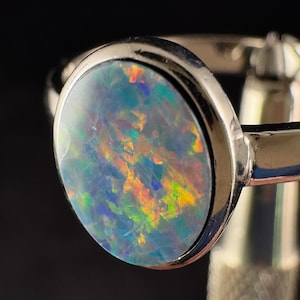 Könnte beinhalten: Ein silberner Ring mit einem runden, schillernden Opal-Edelstein. Der Opal hat eine blaue, grüne und orange Farbe.