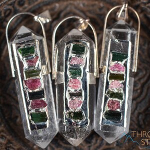 This crystal pendant features a clear Quartz gemstone, showcasing its transparent beauty and amplifying properties. Surrounding the Quartz are seven, green and pink Tourmaline gemstone accent crystals.