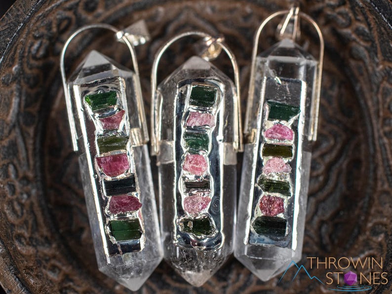 This crystal pendant features a clear Quartz gemstone, showcasing its transparent beauty and amplifying properties. Surrounding the Quartz are seven, green and pink Tourmaline gemstone accent crystals.