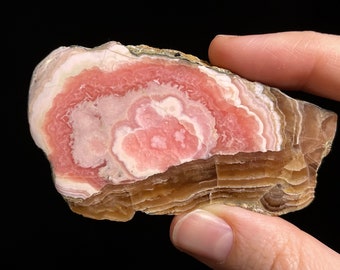 May include: A pink and brown banded agate with a swirling pattern. The agate is a natural stone and has a smooth, polished surface.