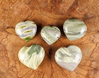 May include: Five green and white heart-shaped stones with swirling patterns on a wooden surface.
