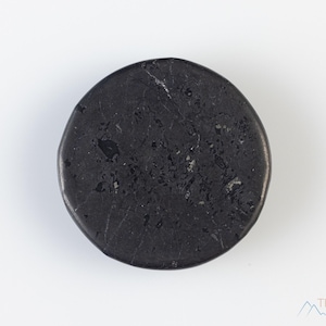 May include: A black, round, smooth stone with a slightly rough texture. The stone is about 2 inches in diameter.