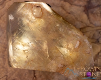 May include: A large, clear, yellow calcite crystal with a rough, natural surface. The crystal has a unique, faceted shape and is translucent.