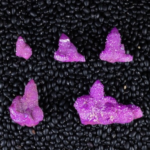 Op de afbeelding: Vijf regenboogkleurige, paarse amethistkristallen op een bed van zwarte bonen.