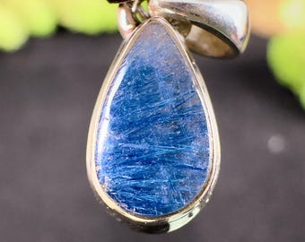 May include: A teardrop-shaped pendant with a vibrant blue gemstone. The stone has a textured appearance with streaks of blue. The pendant is set in a silver-colored metal frame.