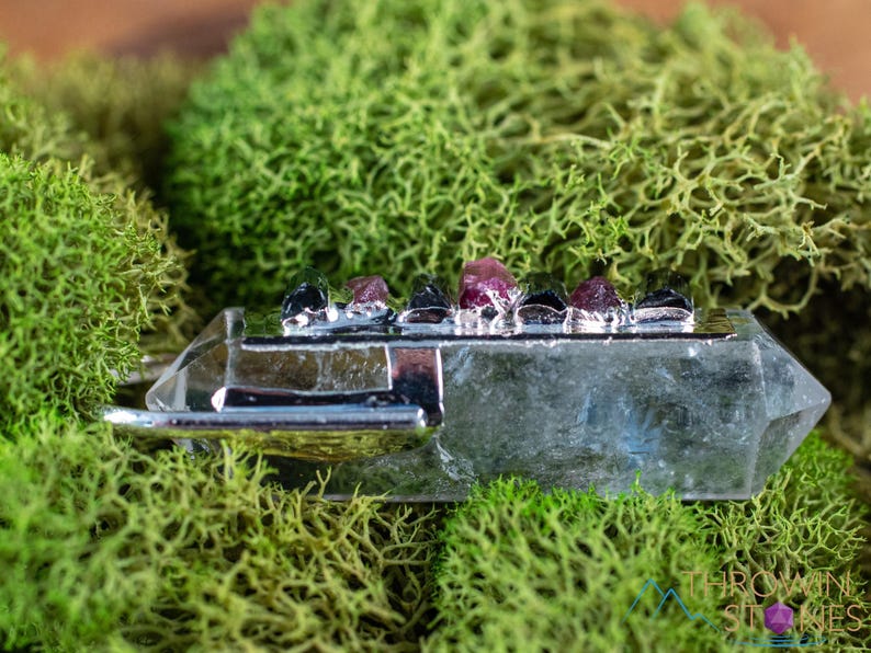 This crystal pendant features a clear Quartz gemstone, showcasing its transparent beauty and amplifying properties. Surrounding the Quartz are seven, green and pink Tourmaline gemstone accent crystals.