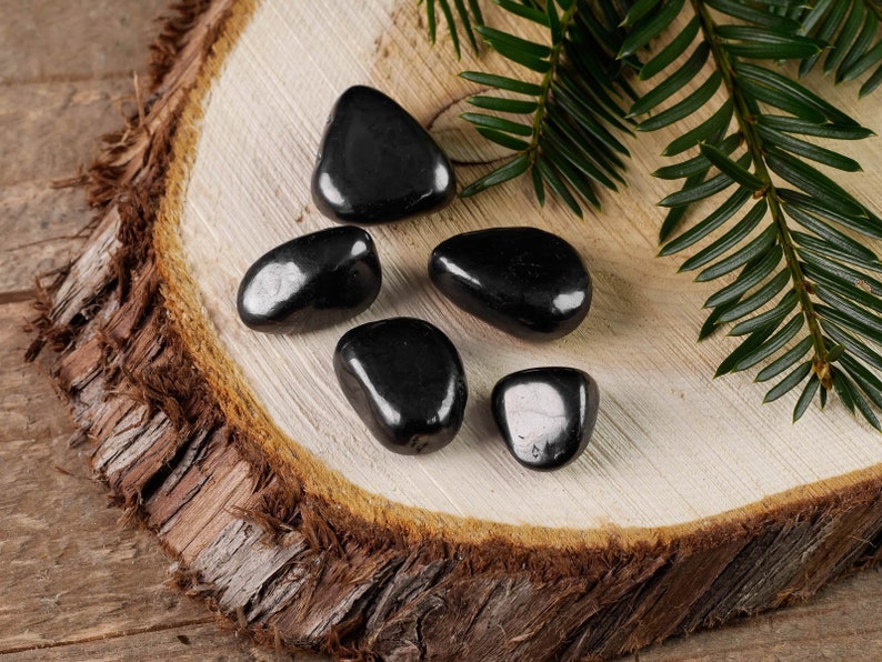 Hematite Tumbled Gemstones. These ethically sourced, semi precious, crystals are black with a polished finish. You will receive 5 stones that are 1.7 to 2.4 centimeters in length and weigh 25 to 35 grams total. Each stone is unique in shape and color