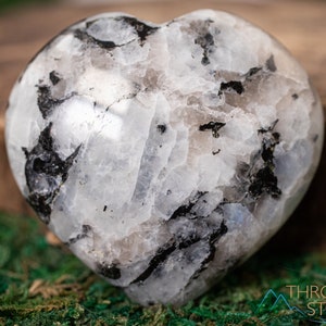 Genuine Moonstone heart shaped crystal. This beautifully hand carved, puffy, palm stone heart, is white with specks of black and rainbow flash. Each crystal heart is unique, and has its own color, shape, and pattern. This listing has variations.