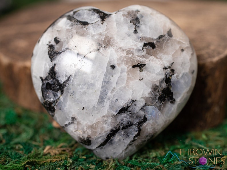 Genuine Moonstone heart shaped crystal. This beautifully hand carved, puffy, palm stone heart, is white with specks of black and rainbow flash. Each crystal heart is unique, and has its own color, shape, and pattern. This listing has variations.