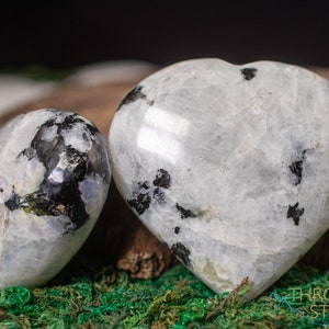 Genuine Moonstone heart shaped crystal. This beautifully hand carved, puffy, palm stone heart, is white with specks of black and rainbow flash. Each crystal heart is unique, and has its own color, shape, and pattern. This listing has variations.