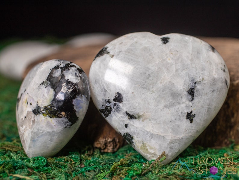 Genuine Moonstone heart shaped crystal. This beautifully hand carved, puffy, palm stone heart, is white with specks of black and rainbow flash. Each crystal heart is unique, and has its own color, shape, and pattern. This listing has variations.