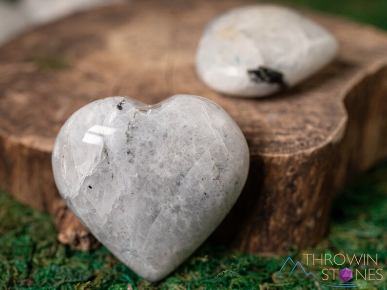 Genuine Moonstone heart shaped crystal. This beautifully hand carved, puffy, palm stone heart, is white with specks of black and rainbow flash. Each crystal heart is unique, and has its own color, shape, and pattern. This listing has variations.