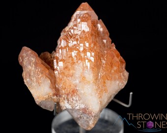 May include: A cluster of orange quartz crystals with a pointed, pyramid-like shape. The crystals are translucent and have a slight reddish hue. The crystals are arranged in a cluster, with some of the crystals pointing upwards and others pointing downwards.