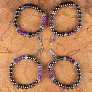 These purple Amethyst and grey Hematite crystal bracelets have round beads strung on elastic.  They feature a silver Goddess Charm.
Crystals are nature-made therefore each one is unique in appearance.