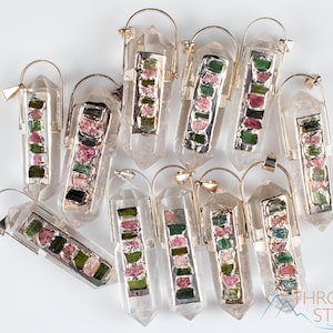 This crystal pendant features a clear Quartz gemstone, showcasing its transparent beauty and amplifying properties. Surrounding the Quartz are seven, green and pink Tourmaline gemstone accent crystals.