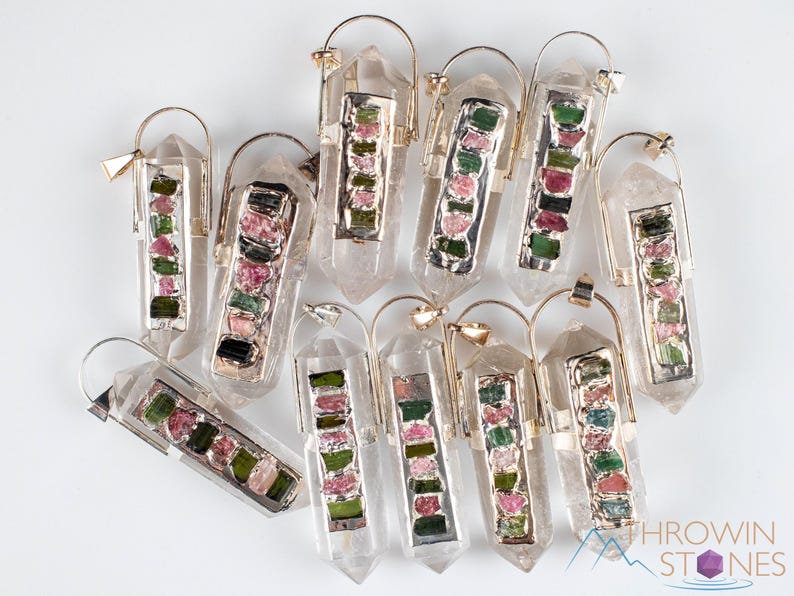 This crystal pendant features a clear Quartz gemstone, showcasing its transparent beauty and amplifying properties. Surrounding the Quartz are seven, green and pink Tourmaline gemstone accent crystals.
