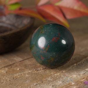 Natural Bloodstone crystal sphere, with wooden stand. This semi-precious, crystal ball is green with red hematite inclusions. Each crystal sphere is beautifully handcrafted, ethically sourced and comes with a wooden stand. This Listing has variations