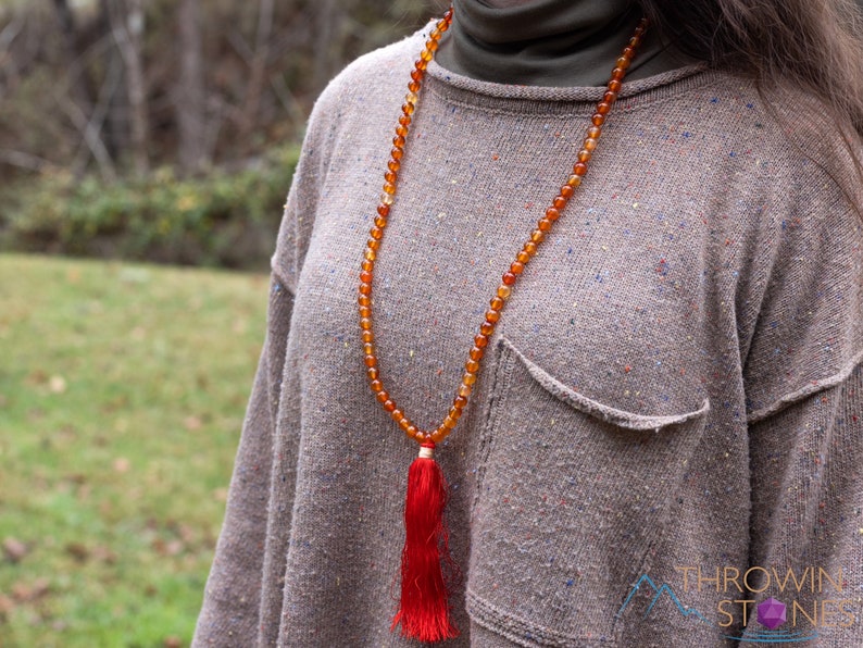 These red orange Carnelian necklaces have 108 sphere beads with a red tassel.  
Crystals are nature-made therefore each one is unique in appearance.