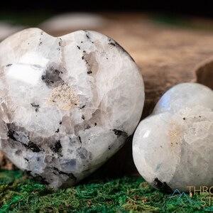 Genuine Moonstone heart shaped crystal. This beautifully hand carved, puffy, palm stone heart, is white with specks of black and rainbow flash. Each crystal heart is unique, and has its own color, shape, and pattern. This listing has variations.