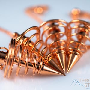 These copper pendulums are wire spirals with a pointed tip, with a copper chain and bead.