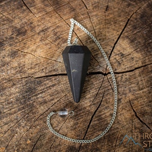 Pode incluir: Pêndulo de obsidiana preta com uma corrente prateada sobre uma superfície de madeira.