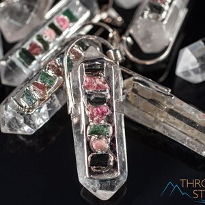 This crystal pendant features a clear Quartz gemstone, showcasing its transparent beauty and amplifying properties. Surrounding the Quartz are seven, green and pink Tourmaline gemstone accent crystals.