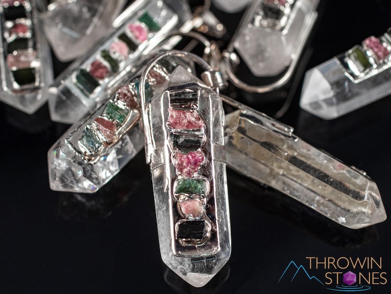 This crystal pendant features a clear Quartz gemstone, showcasing its transparent beauty and amplifying properties. Surrounding the Quartz are seven, green and pink Tourmaline gemstone accent crystals.