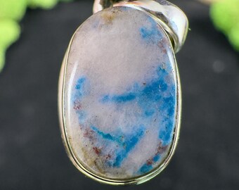 May include: Oval-shaped pendant with a silver-colored bail. The stone features a mix of white, light blue, and brown hues. The stone's surface has a marbled appearance, with the blue creating a striking contrast against the lighter background.