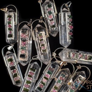 This crystal pendant features a clear Quartz gemstone, showcasing its transparent beauty and amplifying properties. Surrounding the Quartz are seven, green and pink Tourmaline gemstone accent crystals.